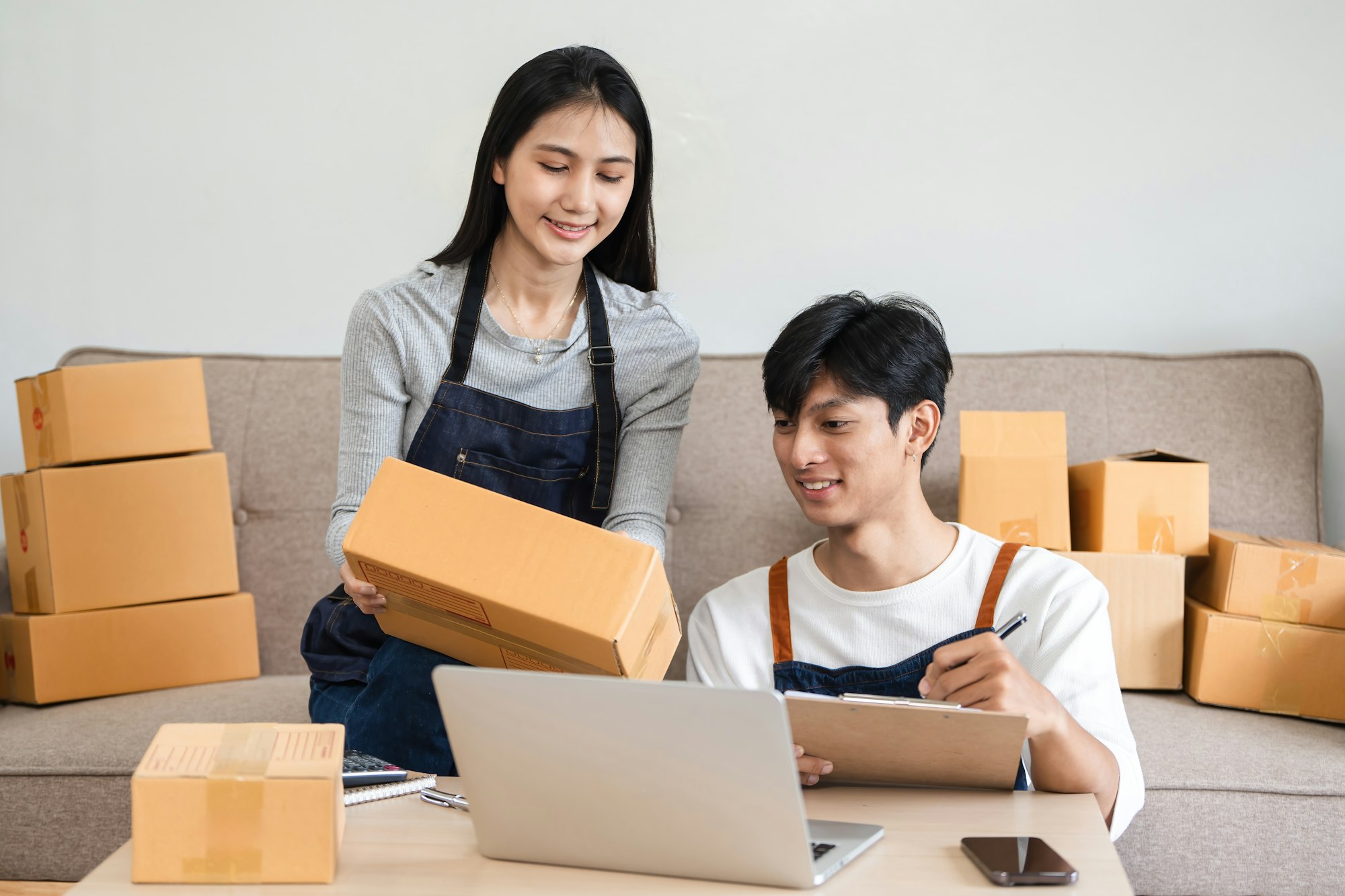 Young Couple Managing Their Small Online Business from Home, Packing Boxes and Using Laptop for